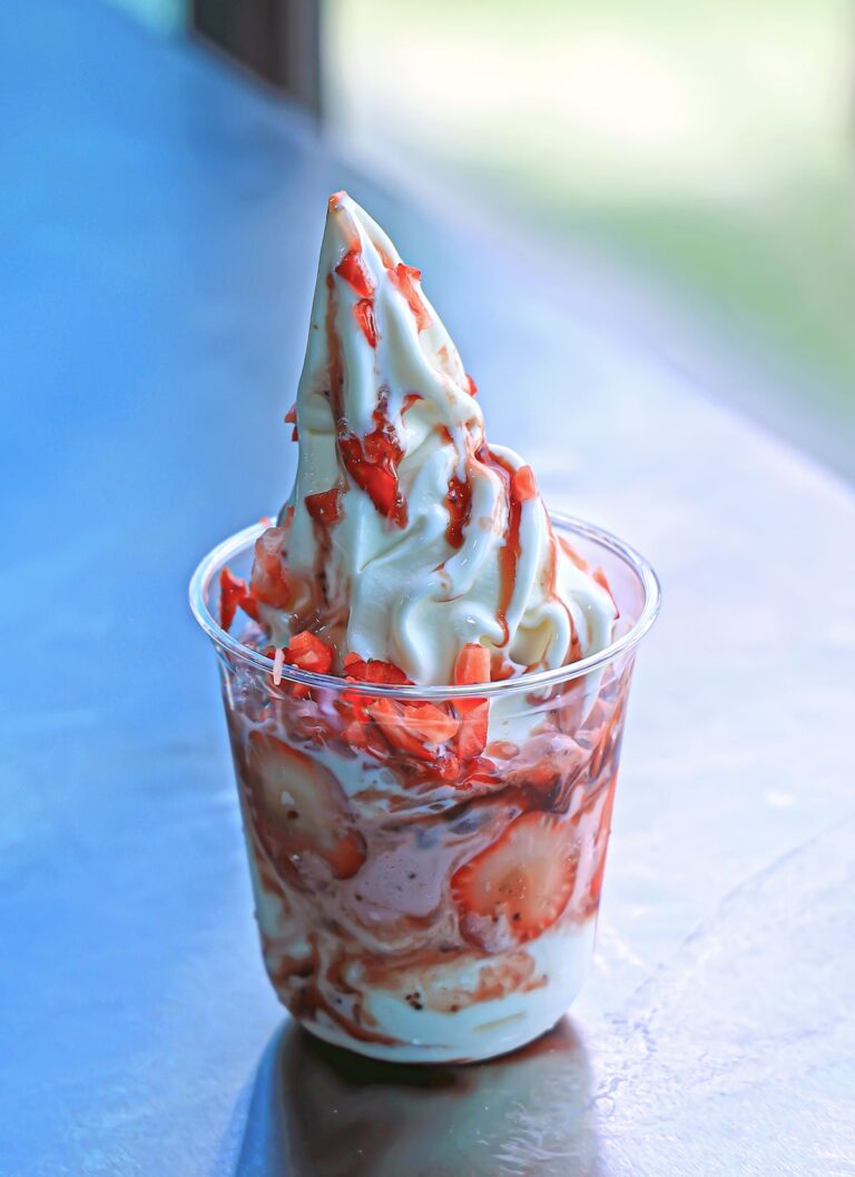 Strawberry soft serve swirl in a clear cup with fresh strawberries